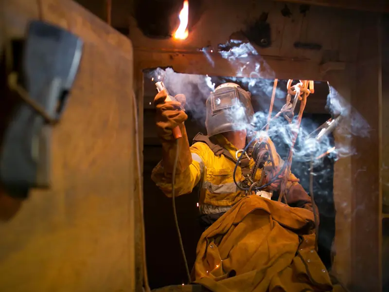 Welder Wearing Protective Gloves And Helmet Works In A Harness