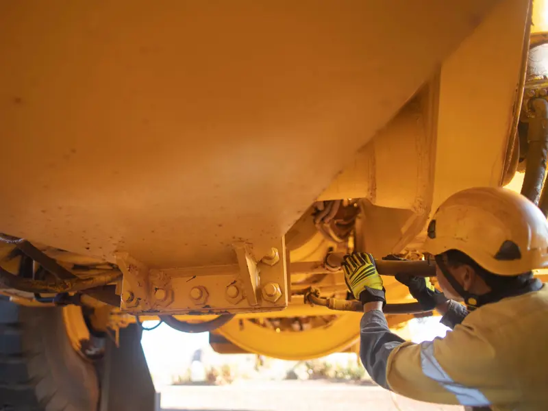 Worker In Hardhat Inspects Underside Of Mining Vehicle